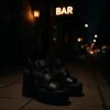 Μαύρες ψηλές πλατφόρμες έξω από bar με βραδινό αστικό φόντο.